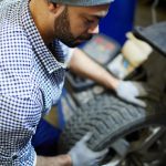 Professional car mechanic with wheel overhauling vehicle